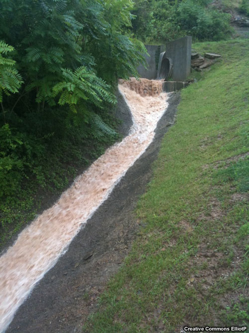 Water pouring out of a culvert and flowing downhill within a paved channel